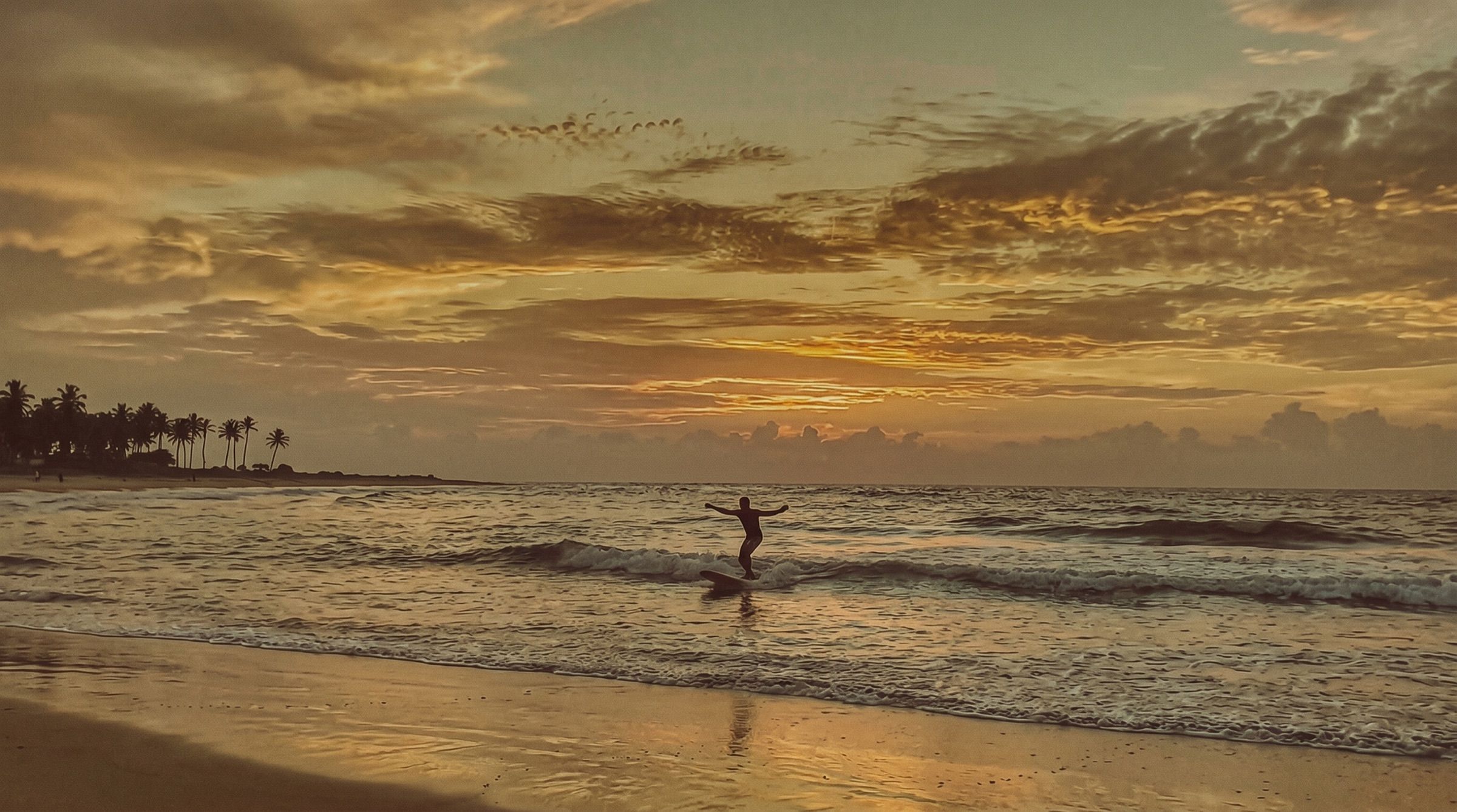 A lone surfer riding a small wave towards the beach at golden hour