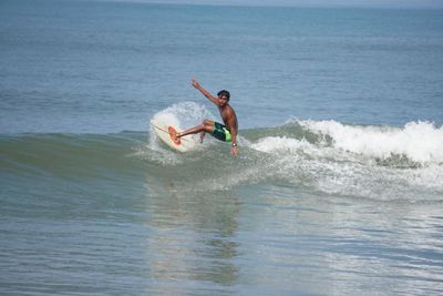 Movin turning off the top of a small wave on a white board, one arm up and spray behind him
