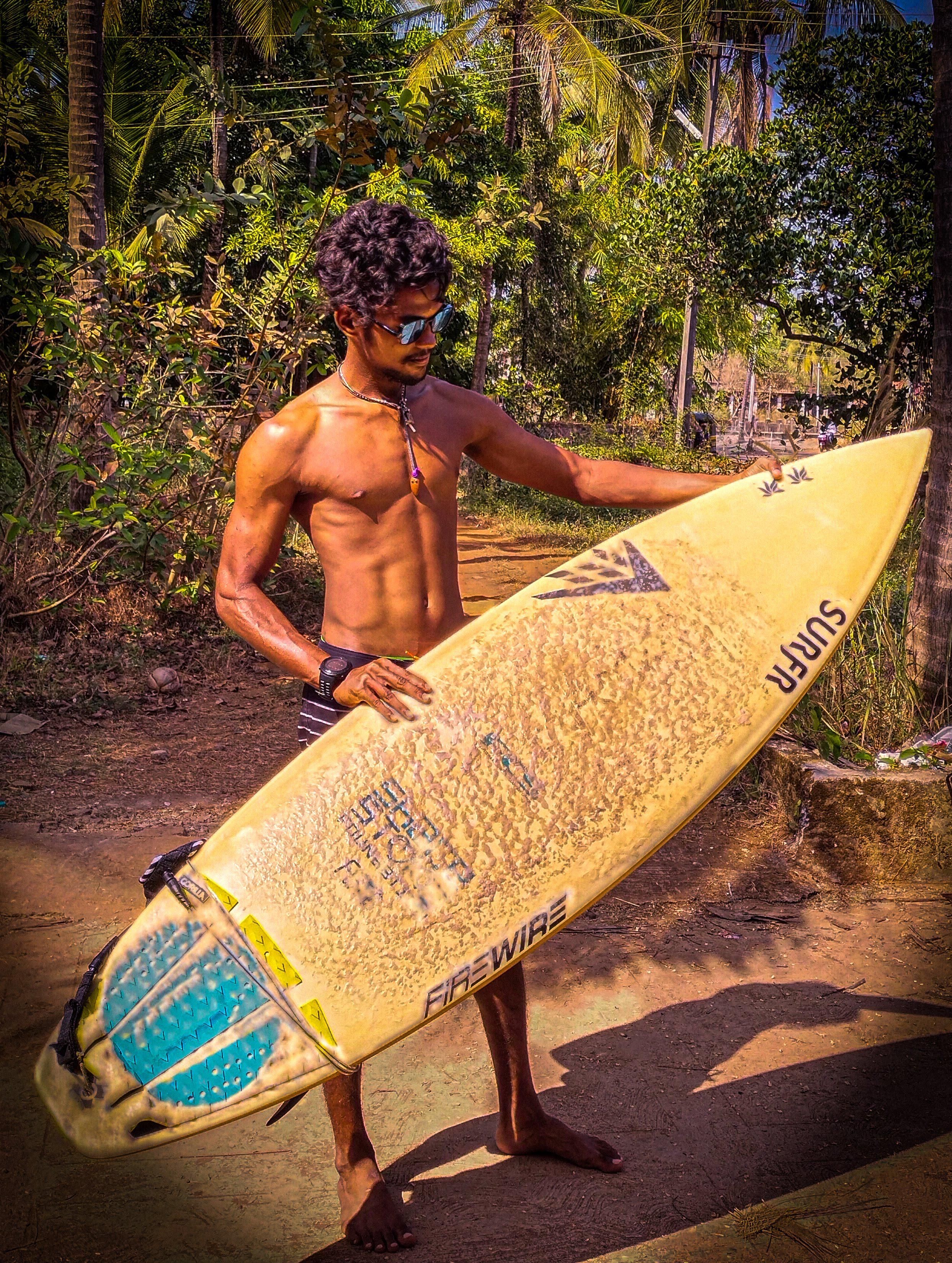 Movin holding a yellow shortboard on a sandy path under palms
