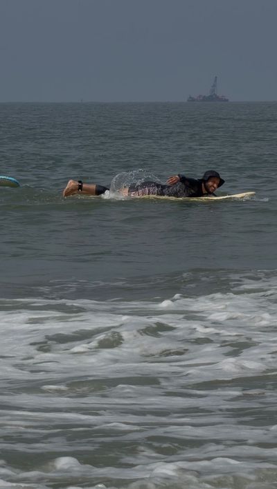Rohan lying on a yellow longboard paddling out through the shorebreak, looking back at the camera