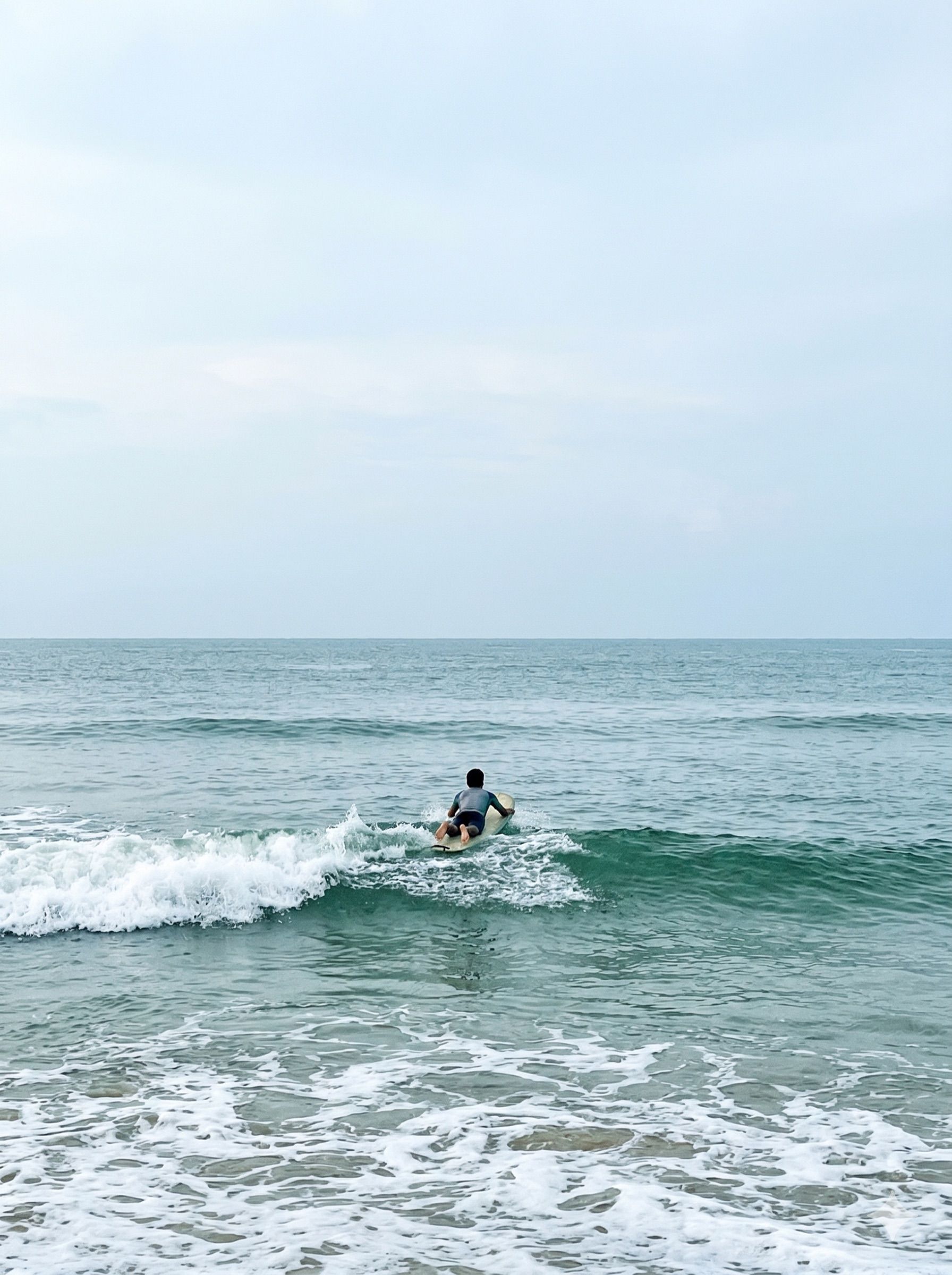 A surfer riding a small wave, seen from a distance along the beach