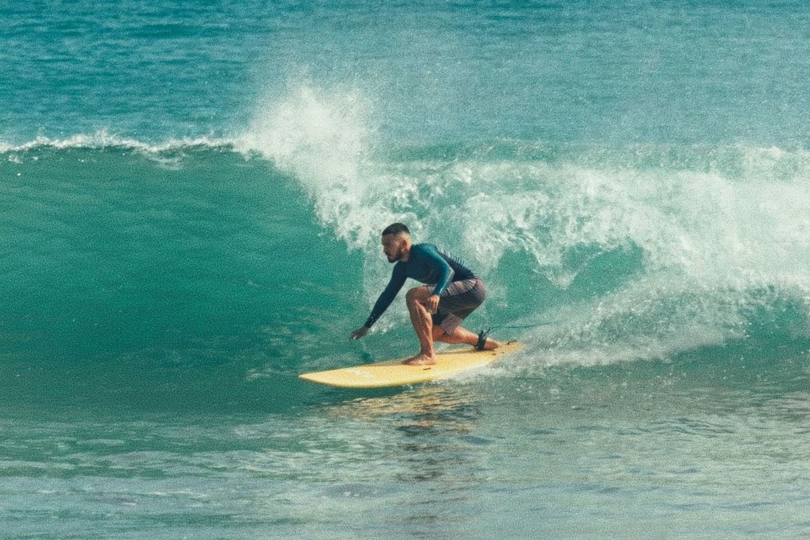 A surfer crouched low on a yellow board inside a green wave at Panambur